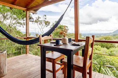 a table and chairs on a porch with a hammock at Cabaña Del Ermitaño entre los árboles del bosque de Efímero la Ceja in La Ceja
