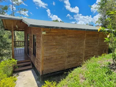 a wooden cabin with a deck in the woods at Cabaña con Jacuzzi cerca al Peñol in Chiquinquirá