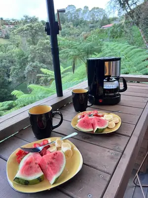 two plates of fruit on a wooden table with two cups at Qimera Ecolodge - Cabaña a 7 Min del Aeropuerto JMC in Guarne