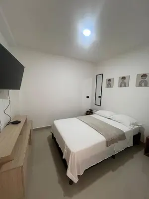 a white bedroom with a bed and a flat screen tv at Apartamento 2 habitaciones en la América in Medellín