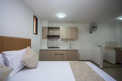 a bedroom with a white bed and a kitchen at Apartahotel Ces in Medellín
