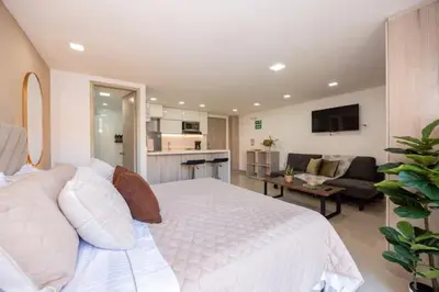 a bedroom with a white bed and a living room at Apartamentos La Frontera in Medellín