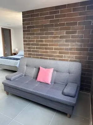 a couch with a pink pillow on it next to a brick wall at Sabaneta, aparta Loft, excelente Ubicacion, Wifi in Sabaneta