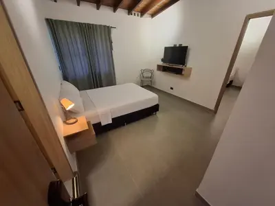 a bedroom with a white bed and a television at Hotel La Casona Estadio in Medellín