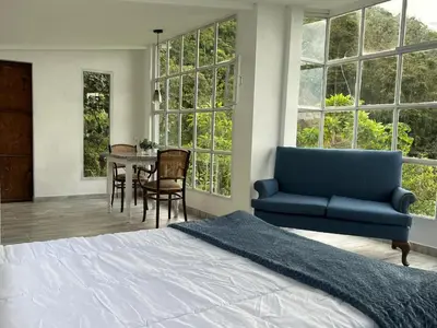 a bedroom with a bed and a table and windows at Entre Nubes y Eucaliptos in Villamaría