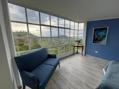 a living room with a blue couch and a large window at Entre Nubes y Eucaliptos in Villamaría