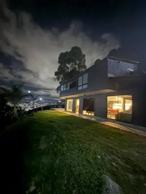 a house with windows on the side of a grass field at Villa with Spectacular Medellin View with Pool and Mini Basket-Futbol Field in Medellín