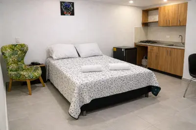 a bedroom with a bed and a chair and a kitchen at Loft con balcón y baño Laureles Belén TOP LOCATION in Medellín