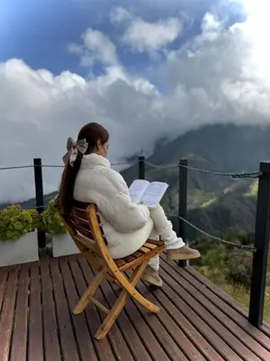a woman sitting in a chair reading a book at EntreNubes Hospedaje de Alta Montaña