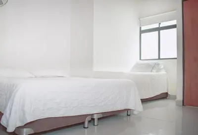 a white bedroom with two beds and a window at Hostel North SAS in Medellín