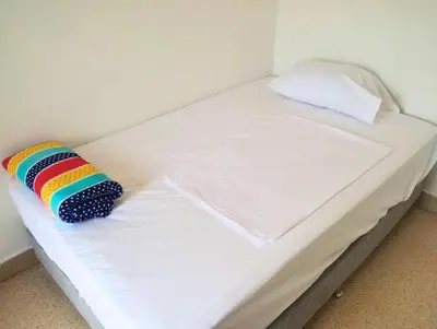 a white bed with a rainbow pillow on it at Cama nueva doble con balcón cerca del parque principal in La Ceja