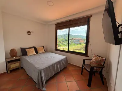 a bedroom with a bed and a window and a chair at Apto nuevo y moderno con piscina y bbq, zona rural in Anserma