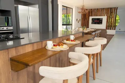 a kitchen with a long counter with white chairs at Villa with Pool, Jacuzzi, and Nature in Medellín