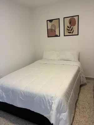 a white bed in a bedroom with two pictures on the wall at El hospedaje de Ana in Medellín