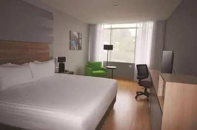 a bedroom with a white bed and a green chair at La Quinta by Wyndham Medellin in Medellín