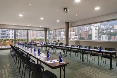 a row of tables and chairs in a room with windows at Hampton by Hilton Medellin in Medellín