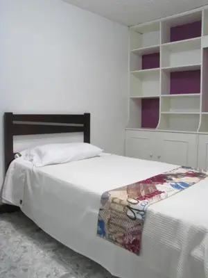 two beds in a bedroom with white walls and shelves at El Cable Hostal in Manizales