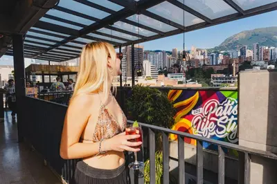 a woman standing on a balcony with a drink at Los Patios Hostel Medellin in Medellín