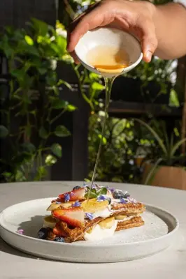 a person drizzling syrup onto a plate of food at Los Patios Hostel Medellin in Medellín