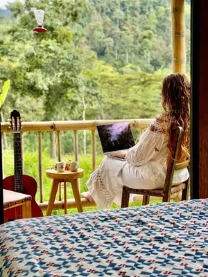 a woman sitting in a chair with a laptop in front of a window at Hacienda Venecia Hostel in Manizales