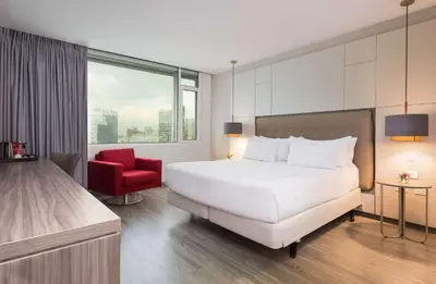 a bedroom with a large white bed and a red chair at NH Collection Medellin Royal in Medellín