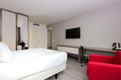 a bedroom with a bed and a desk and a red chair at NH Collection Medellin Royal in Medellín