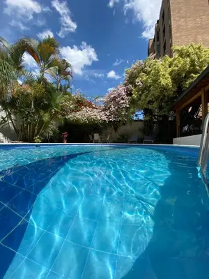 a blue swimming pool with trees and a building at Hotel Portales Del Campestre in Medellín