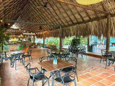 a restaurant with tables and chairs and a straw roof at Los Colores Ecoparque in Doradal