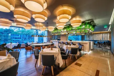 a restaurant with tables and chairs and large windows at Hotel Estelar Milla De Oro in Medellín