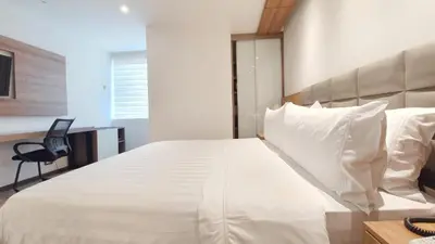 a bedroom with a white bed with a desk and a chair at GHL Hotel Portón Medellín in Medellín
