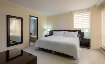 a bedroom with a large white bed and a mirror at GHL Hotel Portón Medellín in Medellín