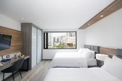 a hotel room with two beds and a desk at GHL Hotel Portón Medellín in Medellín
