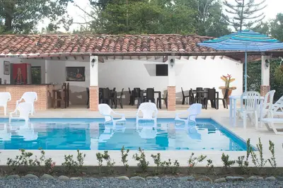 a swimming pool with white chairs and an umbrella at Finca Hotel Guali Santafe in Santa Fe de Antioquia