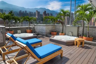 a patio with two lounge chairs and palm trees on a roof at Apartamentos Poblado Alejandría by HOUSY in Medellín