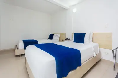 two beds in a white room with blue sheets at Hotel Suite del Parque in Medellín