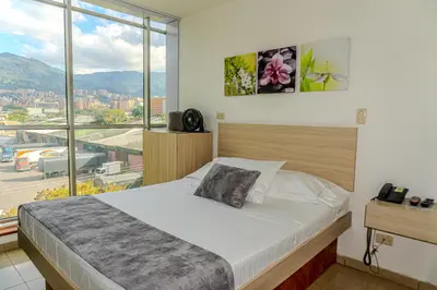 a bedroom with a bed and a large window at Hotel Alcaravan Medellín in Medellín