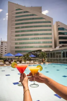 two people holding up cocktails in front of a pool at Hotel San Fernando Plaza in Medellín