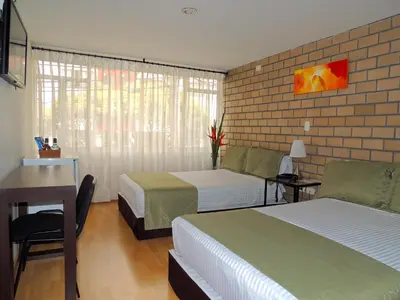 a bedroom with two beds and a desk and a window at Hotel Portal de Milán in Manizales