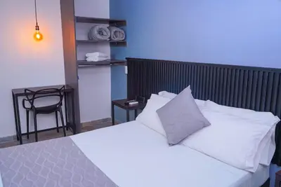 a bedroom with a bed with white sheets and a chair at Hotel Palmas del Estadio in Medellín