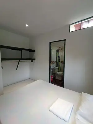 a white bedroom with a bed and a bathroom at Las Cabanas de Pino Hostel in Santa Fe de Antioquia