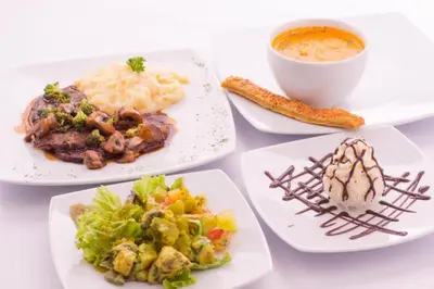 a table with plates of food and a cup of soup at Novelty Suites Hotel - Oviedo Mall in Medellín