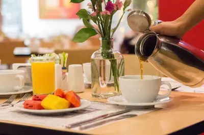 a person is pouring coffee into a cup on a table at Novelty Suites Hotel - Oviedo Mall in Medellín