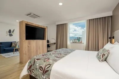 a bedroom with a bed and a television and a couch at Novelty Suites Hotel - Oviedo Mall in Medellín