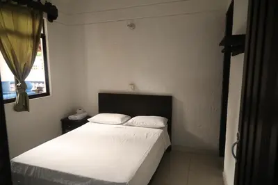 a bedroom with a bed with white sheets and a window at Hospedaje Aquel Almendro in Santa Fe de Antioquia