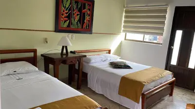 a bedroom with two beds and a table with a lamp at Hotel Tayrona in Puerto Berrío