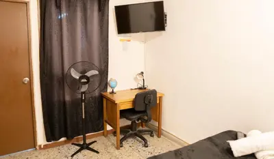 a room with a desk with a fan and a television at Buntes House-Casa Hotel Laureles-Estadio in Medellín