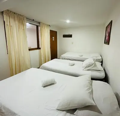 a room with three beds with white sheets and a window at Eco Lodge La Juanita in Manizales
