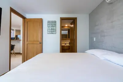 a bedroom with a white bed and a bathroom at Aptos Alcazar Oviedo By HOUSY in Medellín
