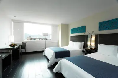 a hotel room with two beds and a desk and a window at Hotel bh El Poblado in Medellín