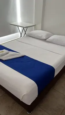 a bed with a blue and white blanket and a table at Hotel Puerto Azul in Puerto Berrío